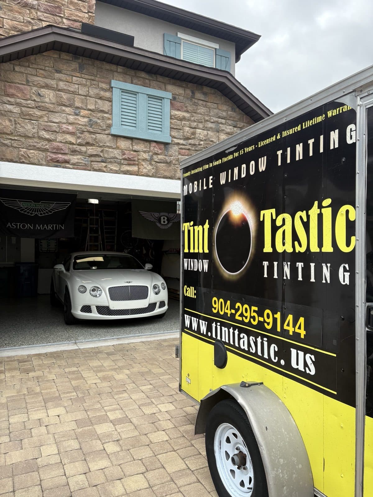 Tint Tastic mobile trailer parked at a customer's home with a Bentley Continental GT visible in the garage